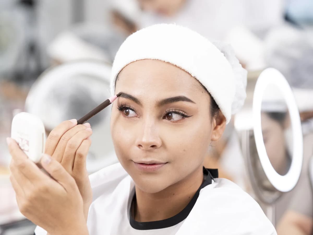 A student shaping her brows at a ring-lit make-up station during a workshop at Adele & Smith